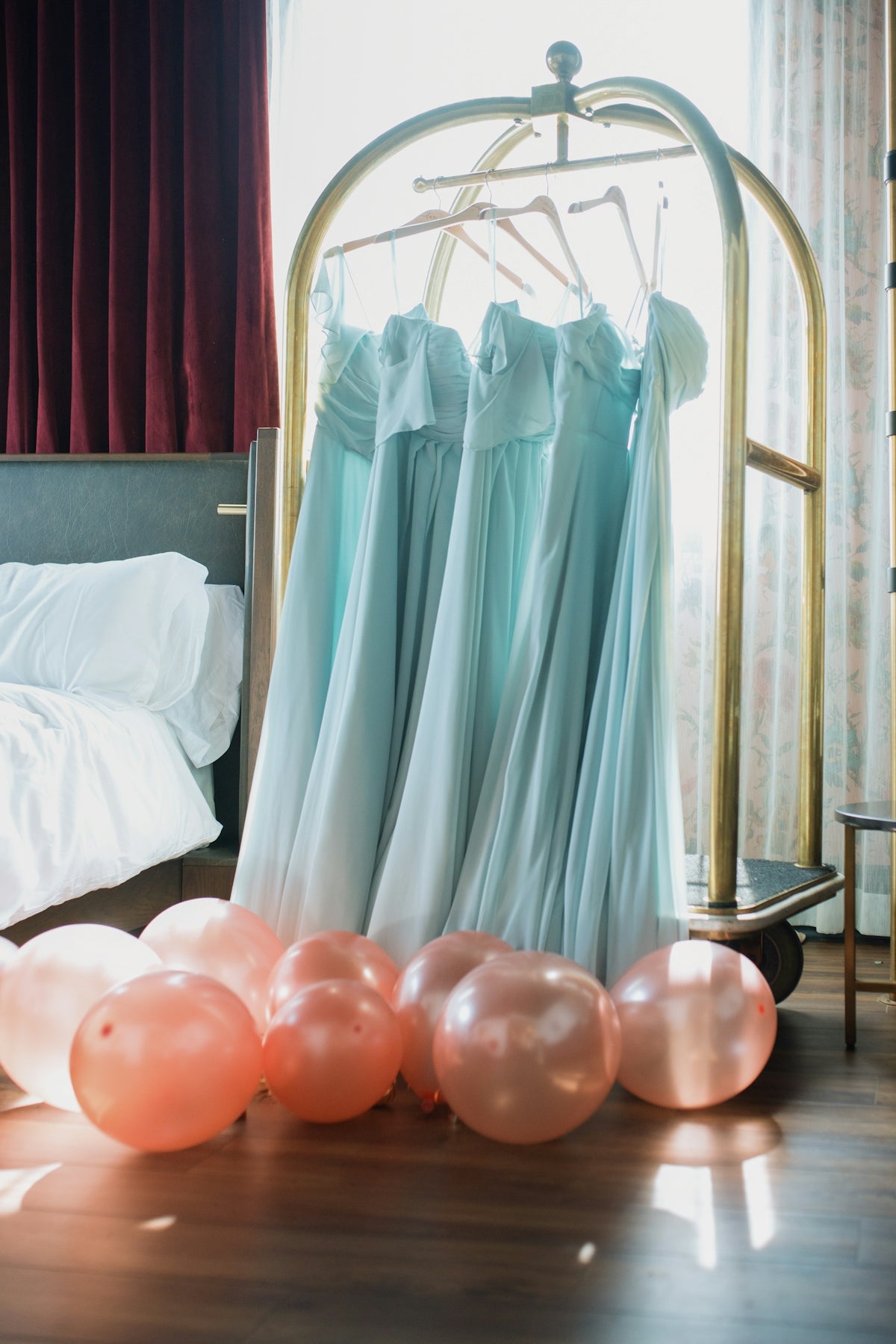 Light blue dresses hang on a luggage cart with balloons.