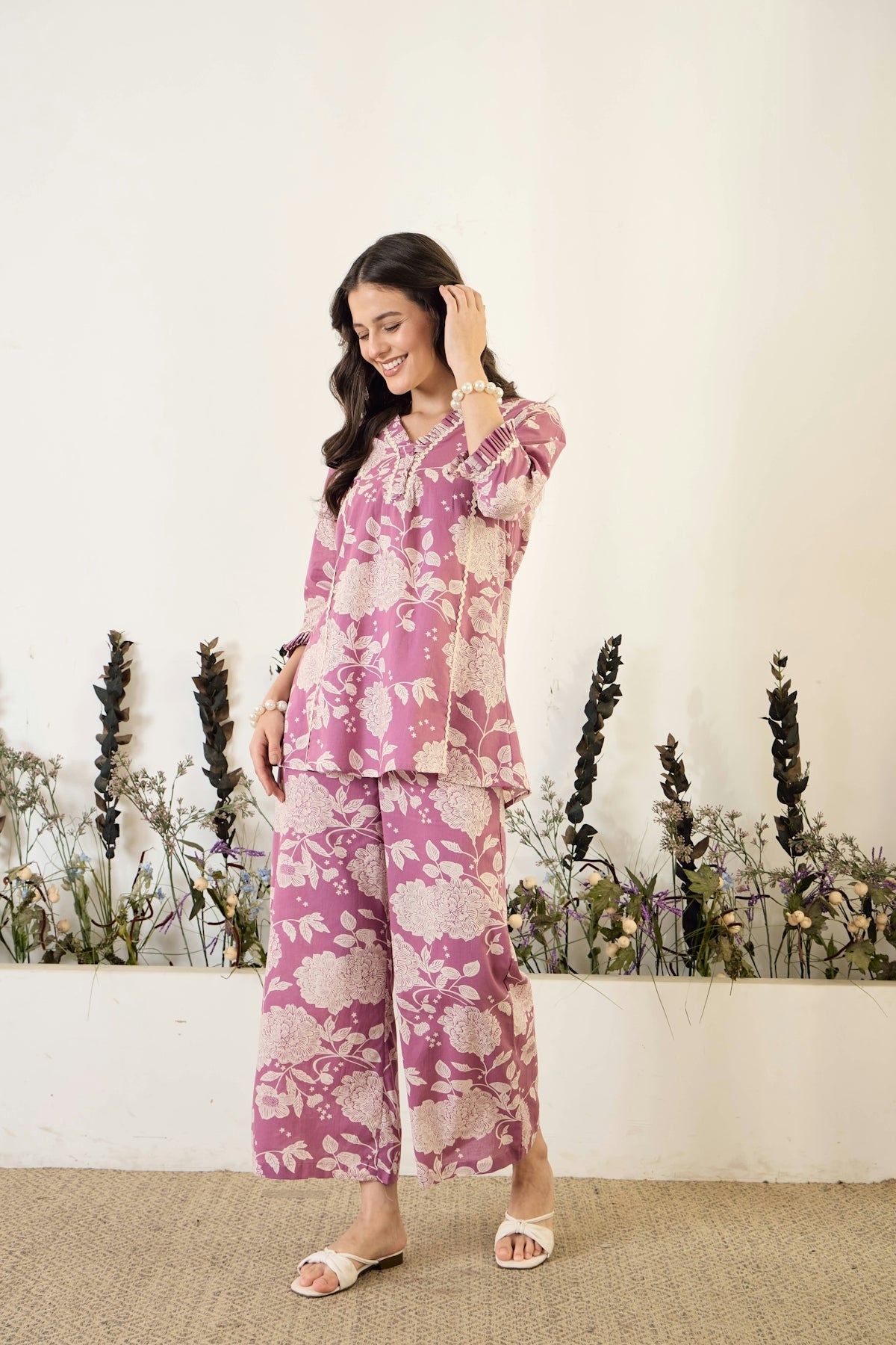 Woman in floral print outfit standing against white wall.